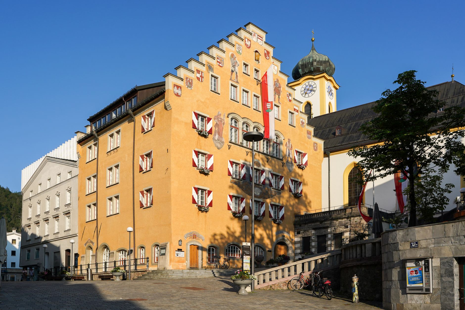 Hall in Tirol's medieval city walls and gate tower viewed from outside, the old town rising behind and the Inn valley stretching away to the west in afternoon light
