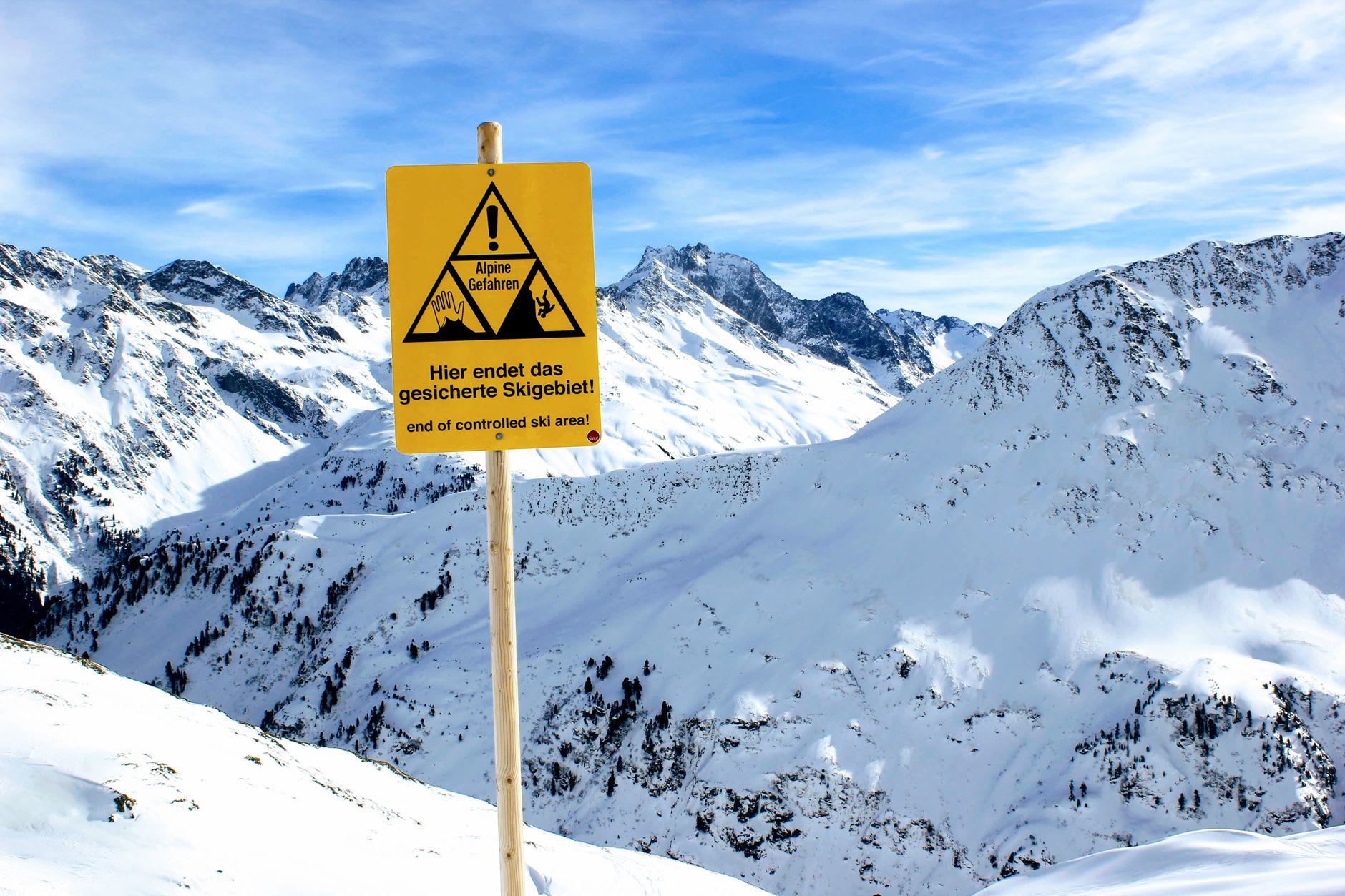Skiers descending a wide groomed piste above St. Anton with jagged Arlberg peaks behind