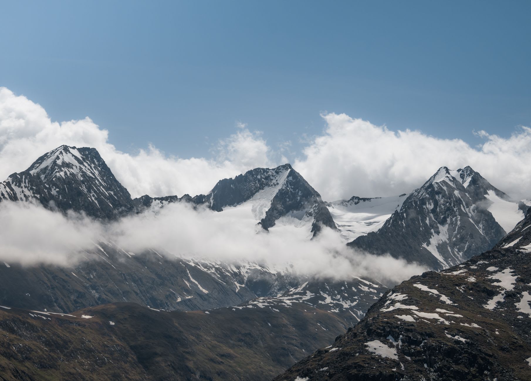 Skiers descending the Stubai Glacier snowfield in August sunshine with the crevassed lower glacier and the rocky peaks of the Stubai Alps behind