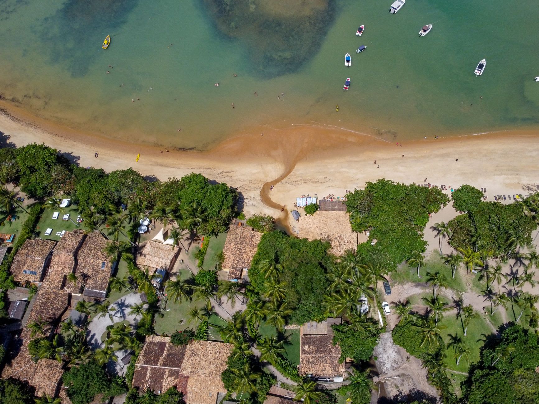 The beach below Trancoso's clifftop village, wide and uncrowded at low tide with palm fronds in the foreground