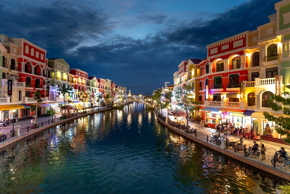 Canal-side restaurants and outdoor seating along the Amwaj Islands boardwalk at dusk with the water reflecting string lights