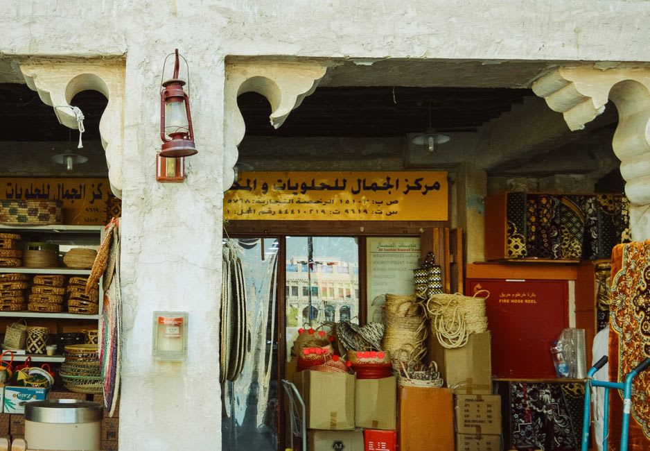 Narrow alley in Manama Souq lined with textile and spice shops, early morning light and a shopkeeper arranging goods
