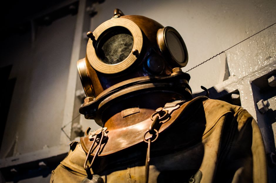 Artefactos tradicionales de buceo de perlas incluyendo pinzas de nariz, cestas y fotografías en blanco y negro exhibidas en una vitrina del museo