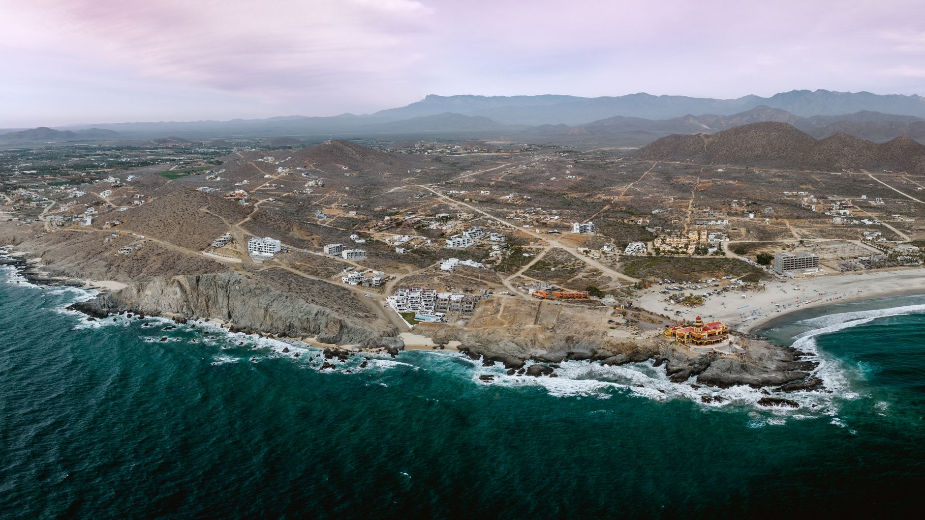 Una hilera de pangas pesqueras varadas en la playa de Los Barriles al amanecer, el Mar de Cortés plano y plateado con la primera luz y las montañas del Cabo del Este detrás
