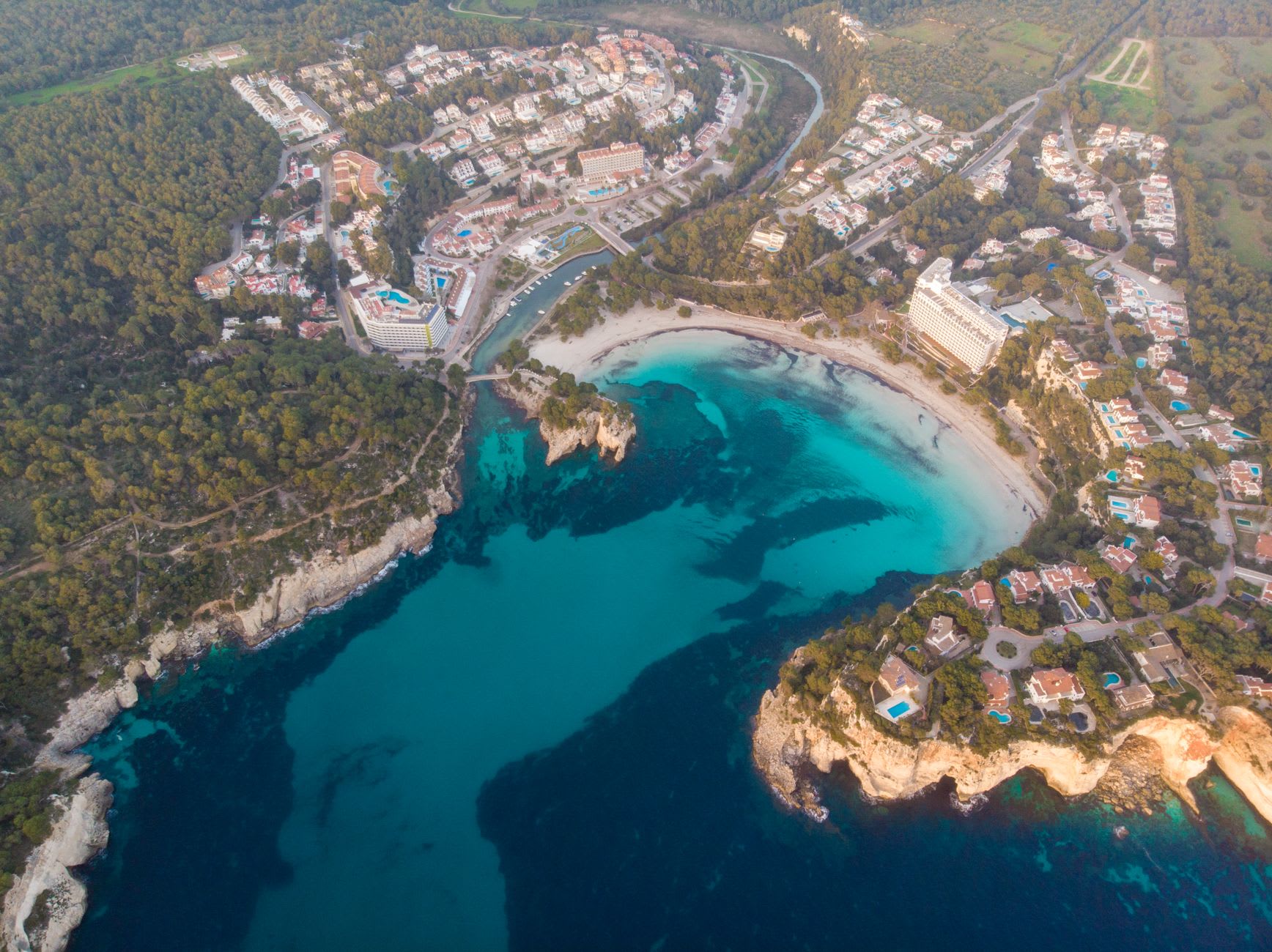Red-earth tracks through pine and carob forest in Ibiza's rural north, the sea visible in flashes through the trees