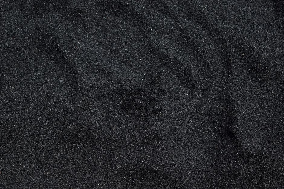 Close-up of black volcanic sand on Lovina beach with a fishing boat in soft morning light