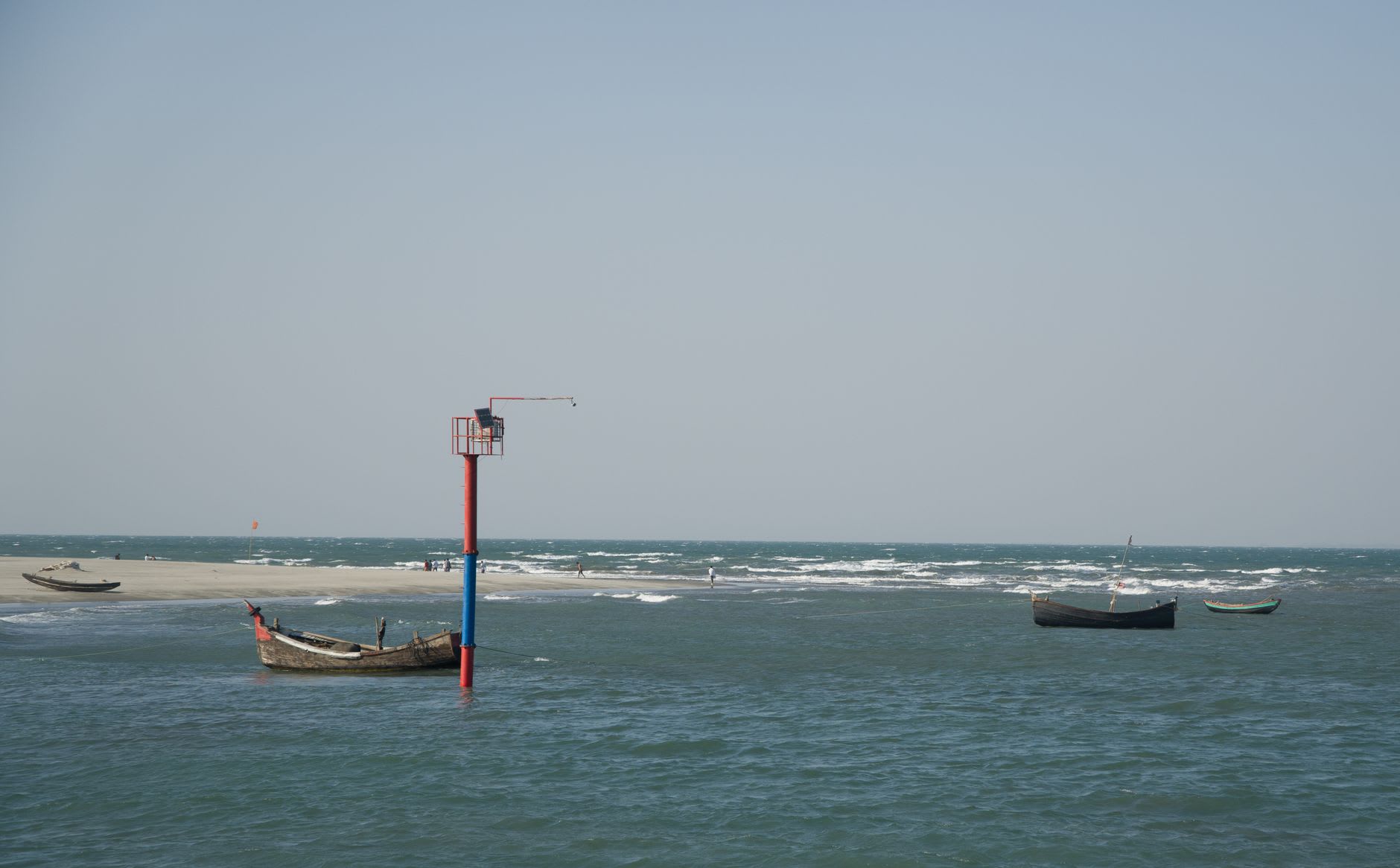 Wooden fishing boats and a cluster of food stalls on the sand near the jetty at Saint Martin's Island, busy with day visitors under coconut palms.