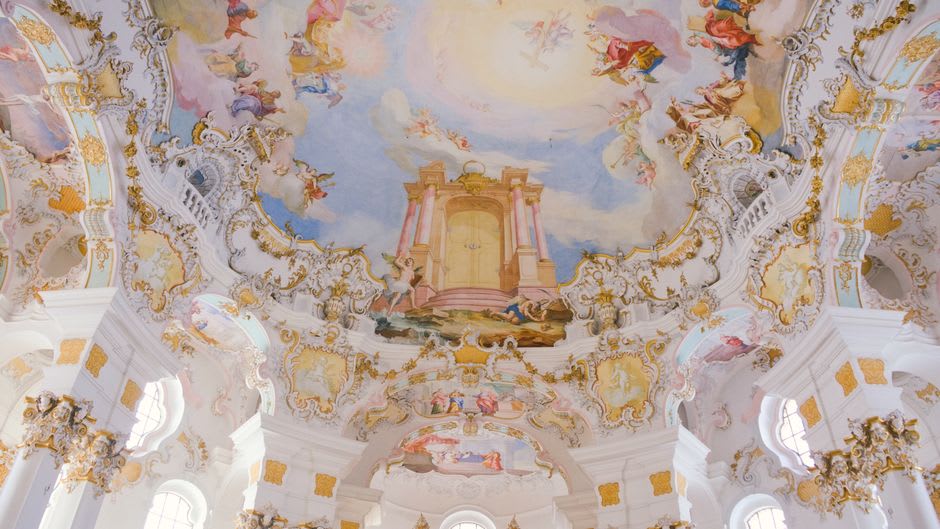 Ornate Rococo ceiling fresco inside the Wieskirche with swirling clouds and golden light