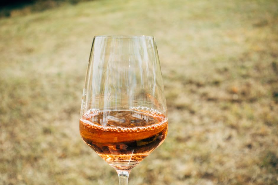 Una copa de vino rosado en la terraza de Chateau Kefraya, con viñedos y montañas lejanas visibles detrás