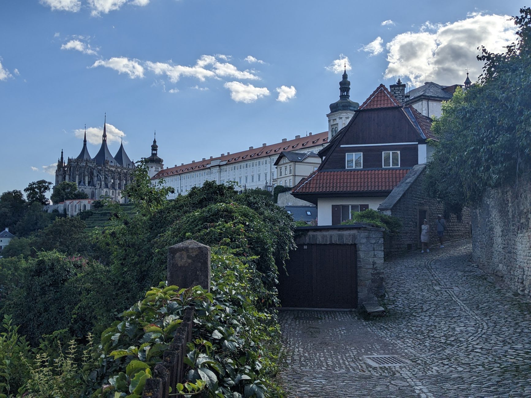 The inner courtyards and stepped fortifications of Karlstejn Castle climbing the wooded hill, stone walls and red roofs rising toward the Great Tower