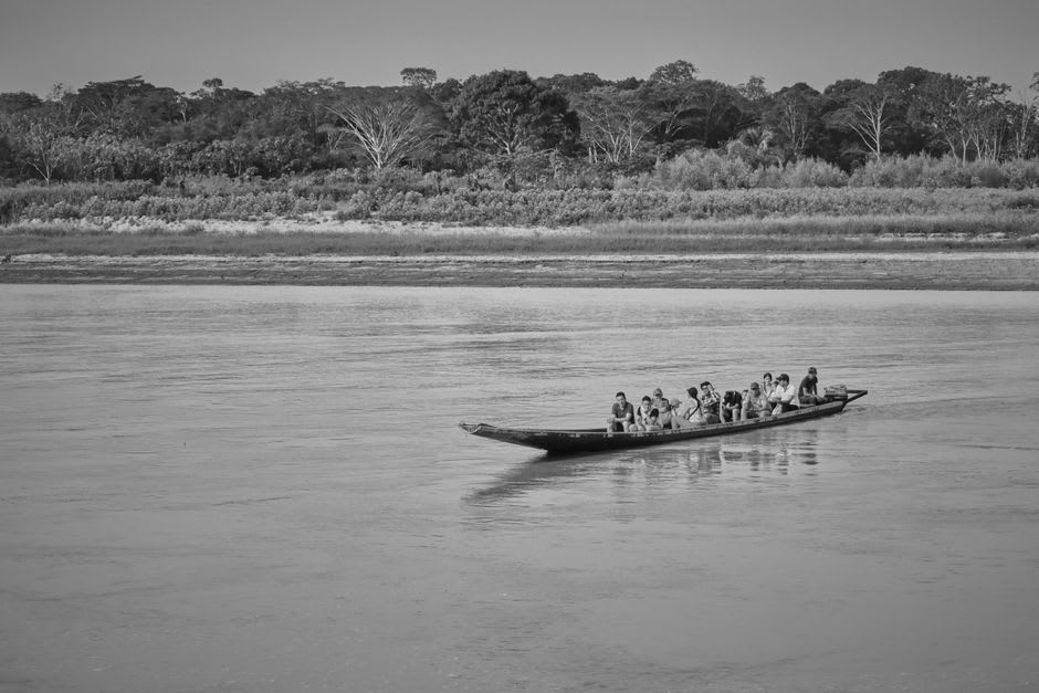 A wooden longboat navigating the Tuichi River surrounded by dense rainforest