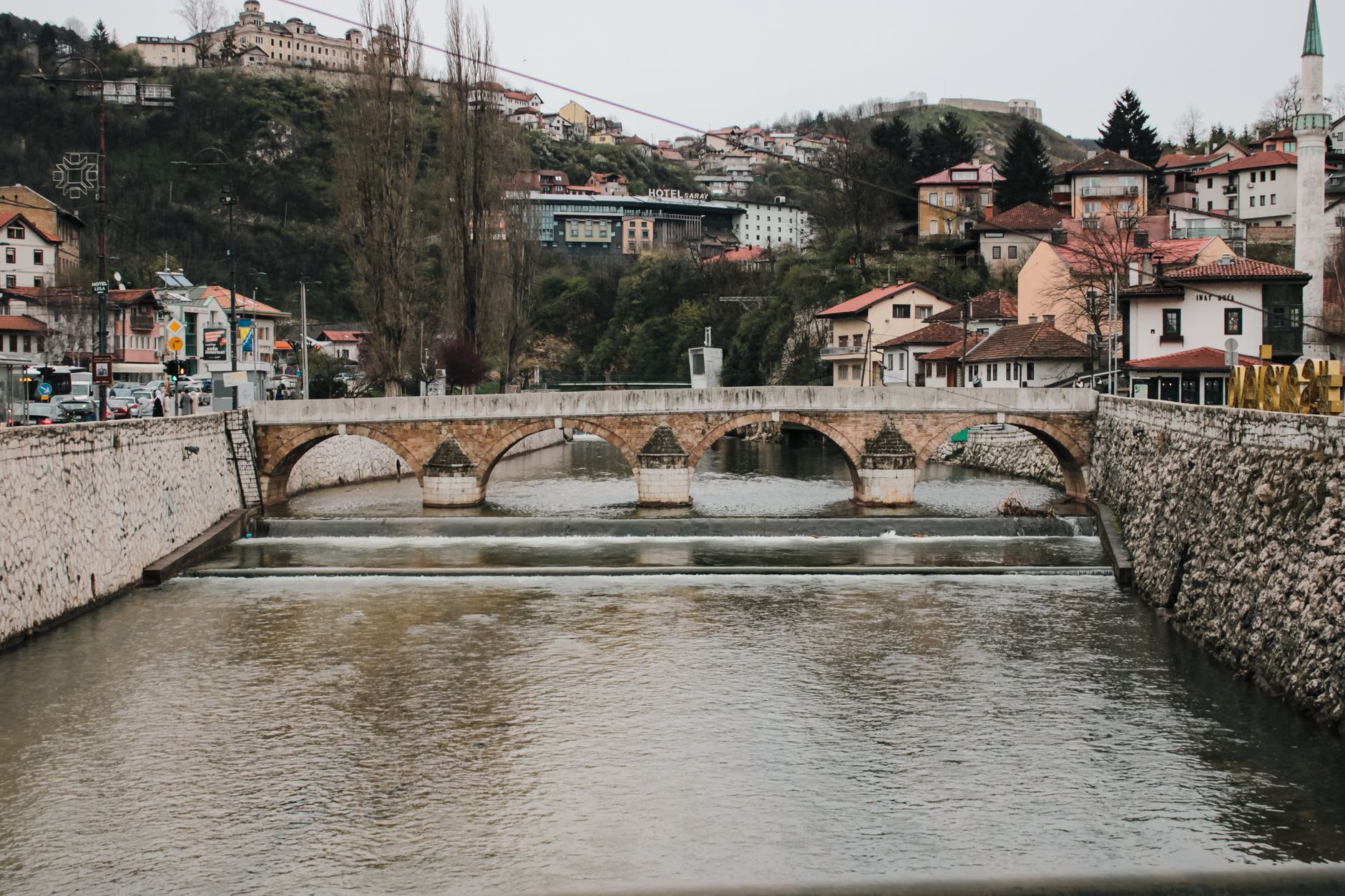The Stara Ćuprija bridge in Konjic seen from the riverbank, its stone arch reflected in the green Neretva below
