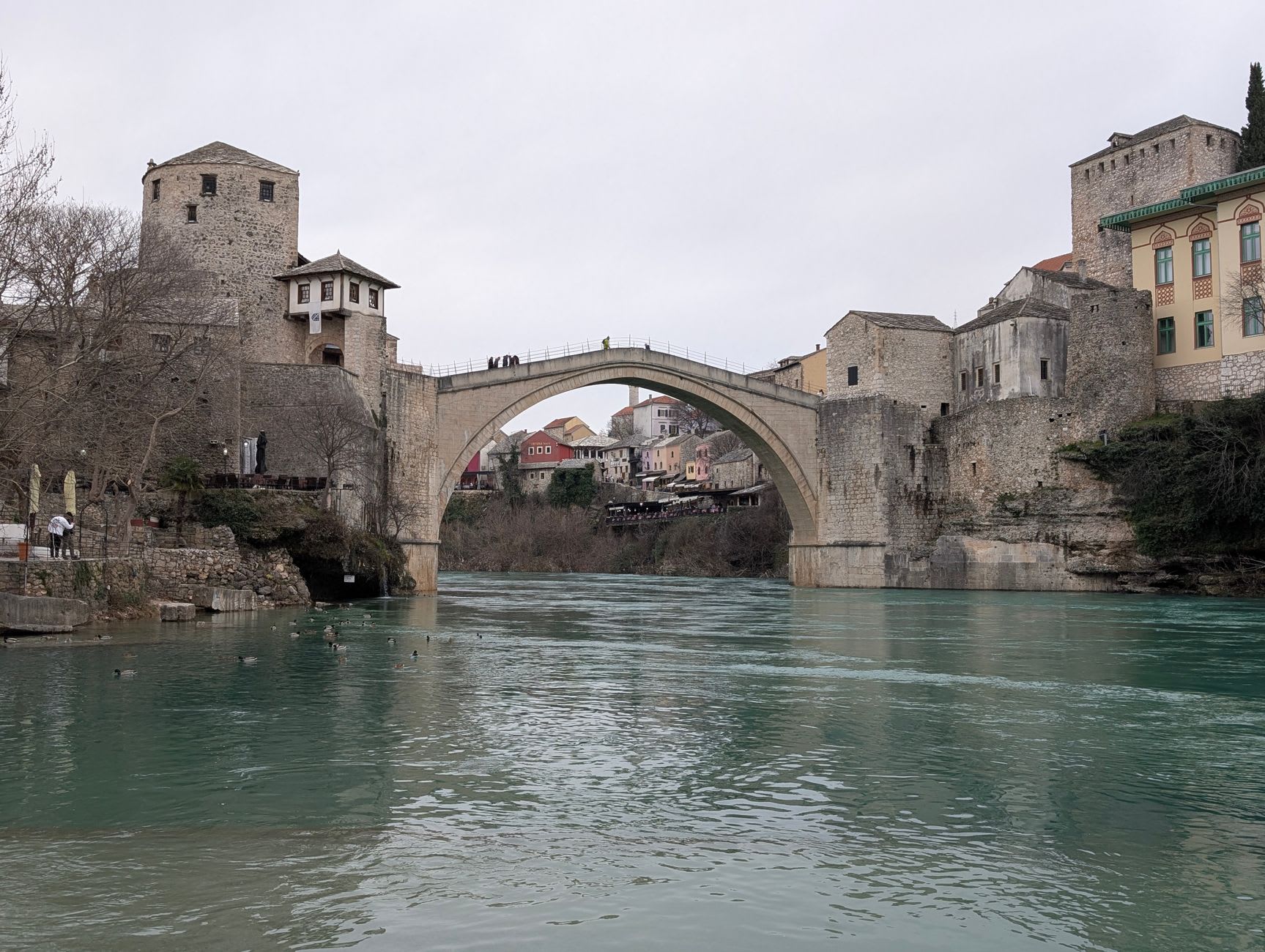 The Neretva river seen from the old bridge, its improbable green water running between stone banks and terraced cafés
