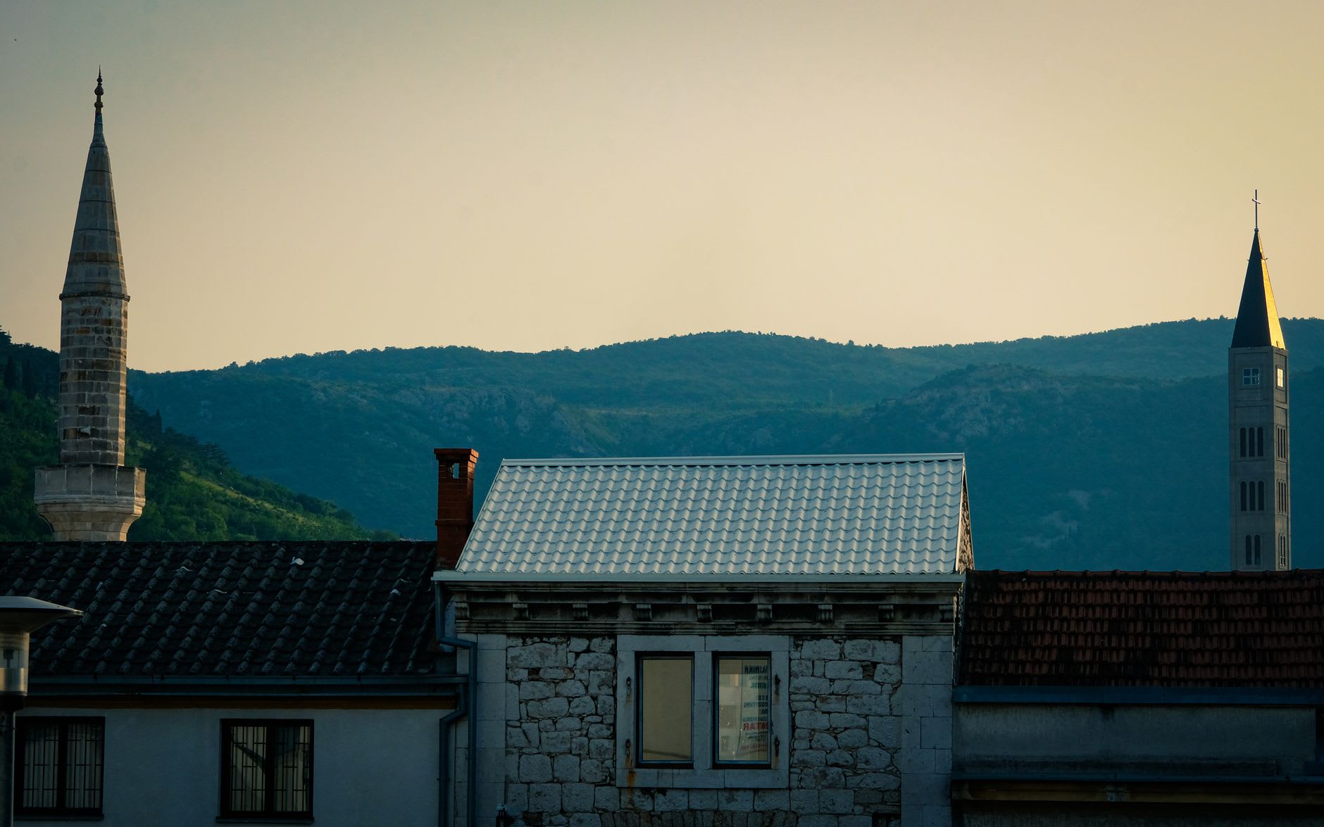 The clock tower and mosque minaret rising above Počitelj's stone rooftops, the Neretva valley spreading wide below