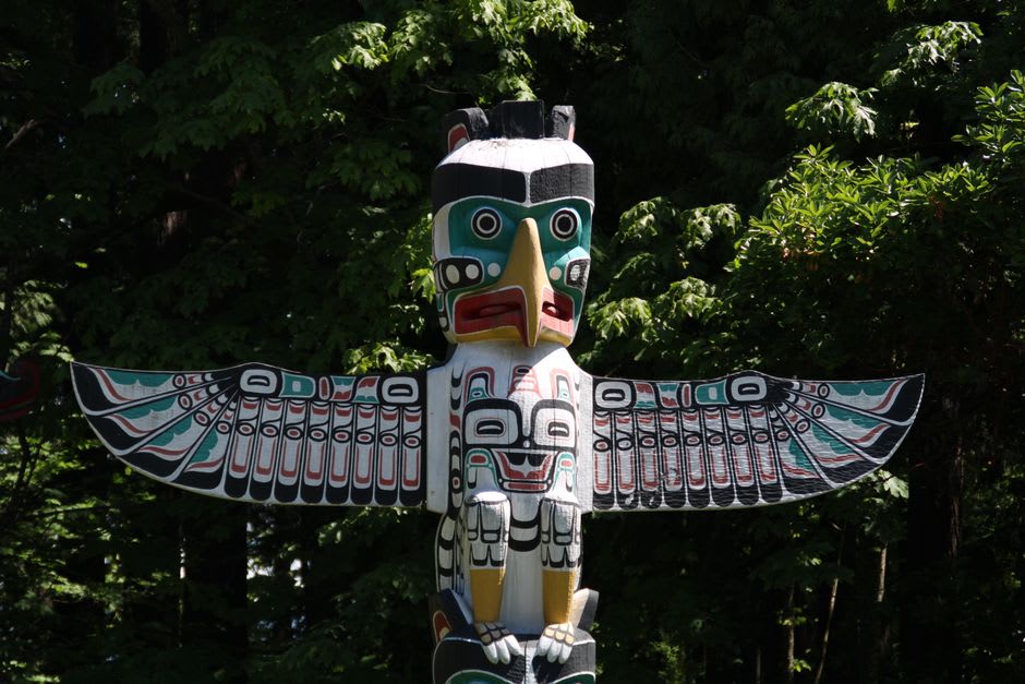 A totem pole carved in Tsimshian style standing near Prince Rupert's waterfront, weathered by coastal rain and fog