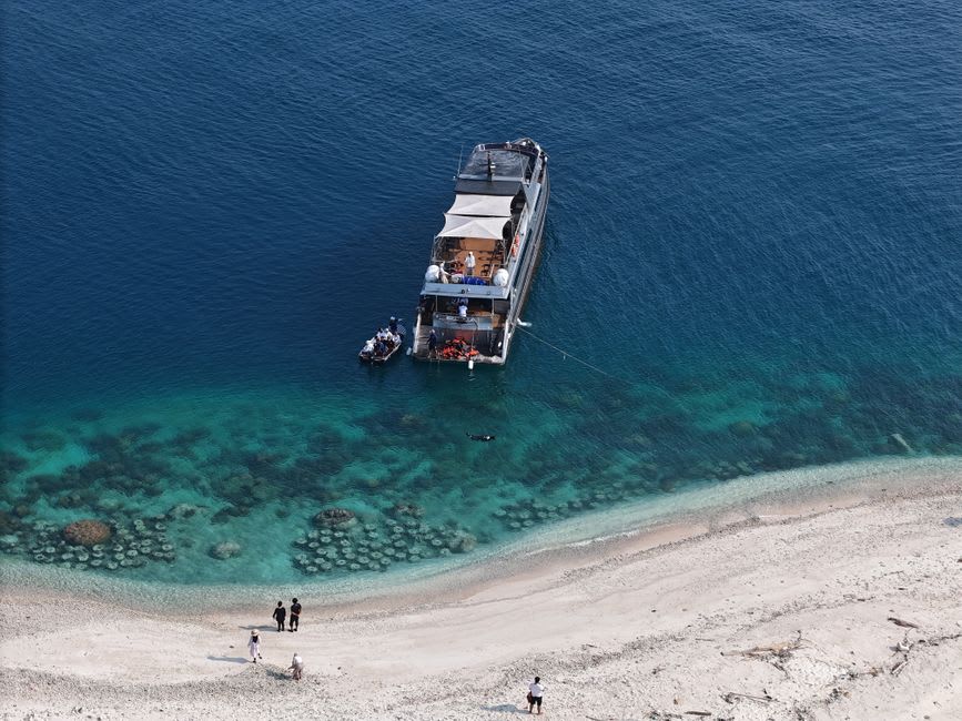 La petite plage de sable de Marina Cay avec un bateau de plongée amarré juste au large et le récif visible sous une eau claire