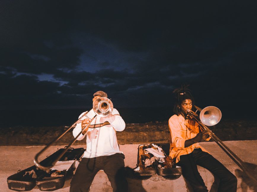 Músicos de tambores de acero tocando en la playa de Trellis Bay de noche con el resplandor de las esculturas de fuego reflejado en el agua detrás de ellos