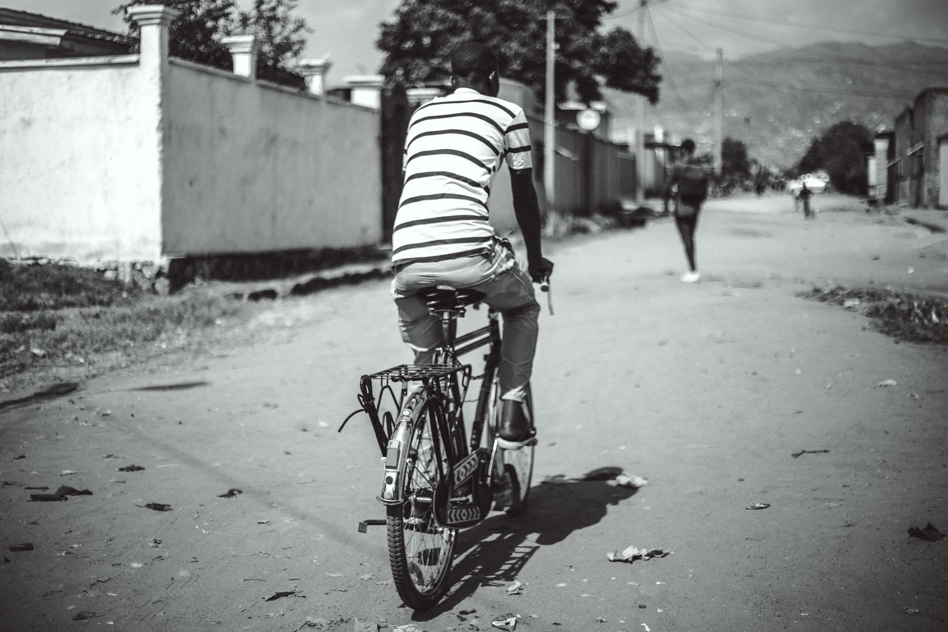 Escena callejera en el centro de Bujumbura — un puesto de vendedor lleno de productos tropicales, una boda-boda abriéndose paso en el calor de la tarde