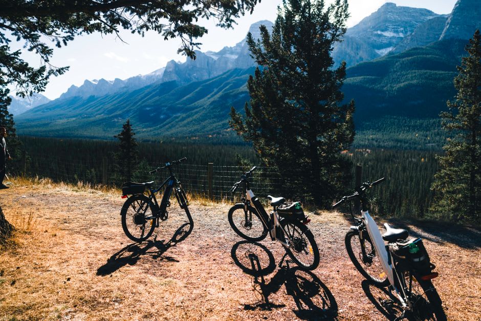 Cyclists riding a forested trail with mountain peaks visible through the trees near Canmore