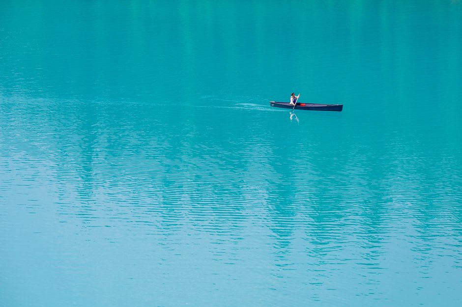 Canoe gliding across a turquoise quartzite lake framed by pink granite ridges