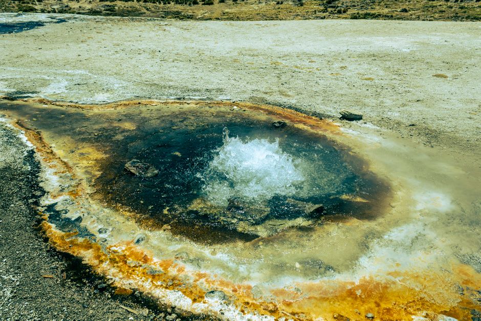 Vivid rust-orange ochre pools at the Paint Pots surrounded by dense green forest