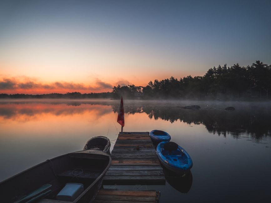 Canoe resting on the still shoreline of Clear Lake at sunrise with forested hills behind