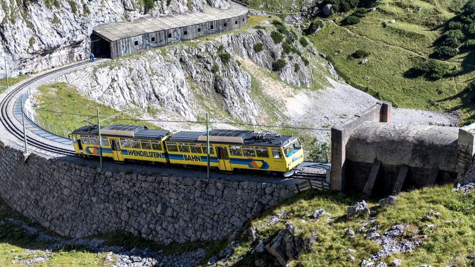 Freight train emerging from a tunnel portal partway up a forested mountainside at the Spiral Tunnels