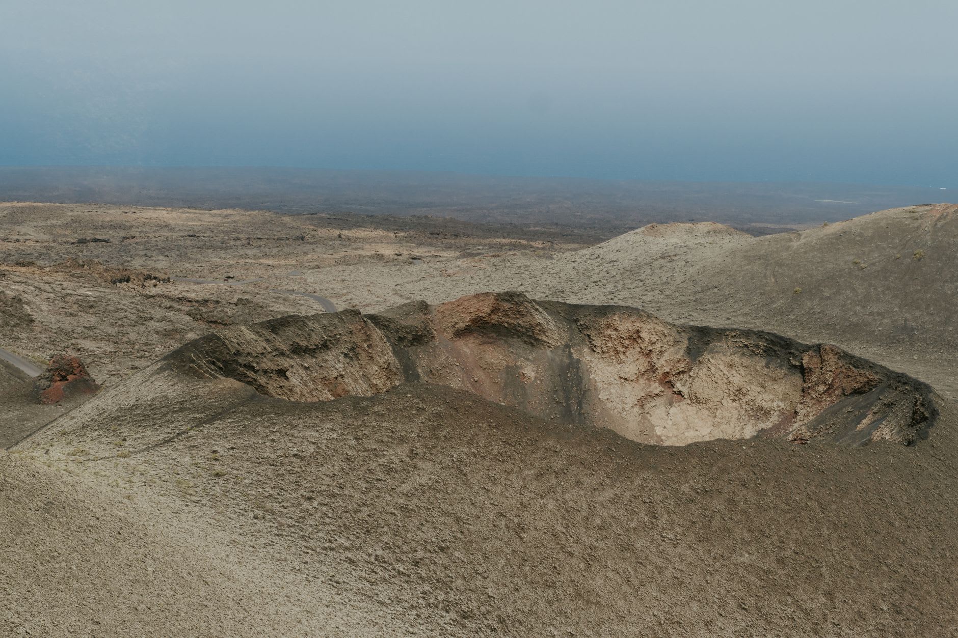 Hardened lava flows in red, black and ochre stretching across the Timanfaya volcanic landscape toward distant fire mountain cones