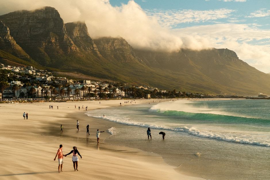 Sunbathers and beachgoers on Camps Bay's white sand with the Twelve Apostles mountains behind them