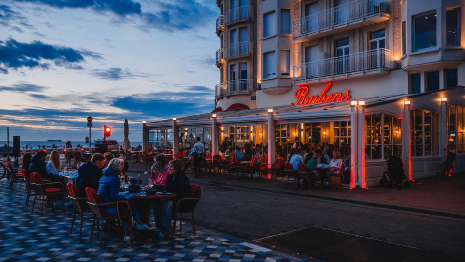 Palm trees lining Victoria Road promenade at sunset with restaurant terraces facing the beach