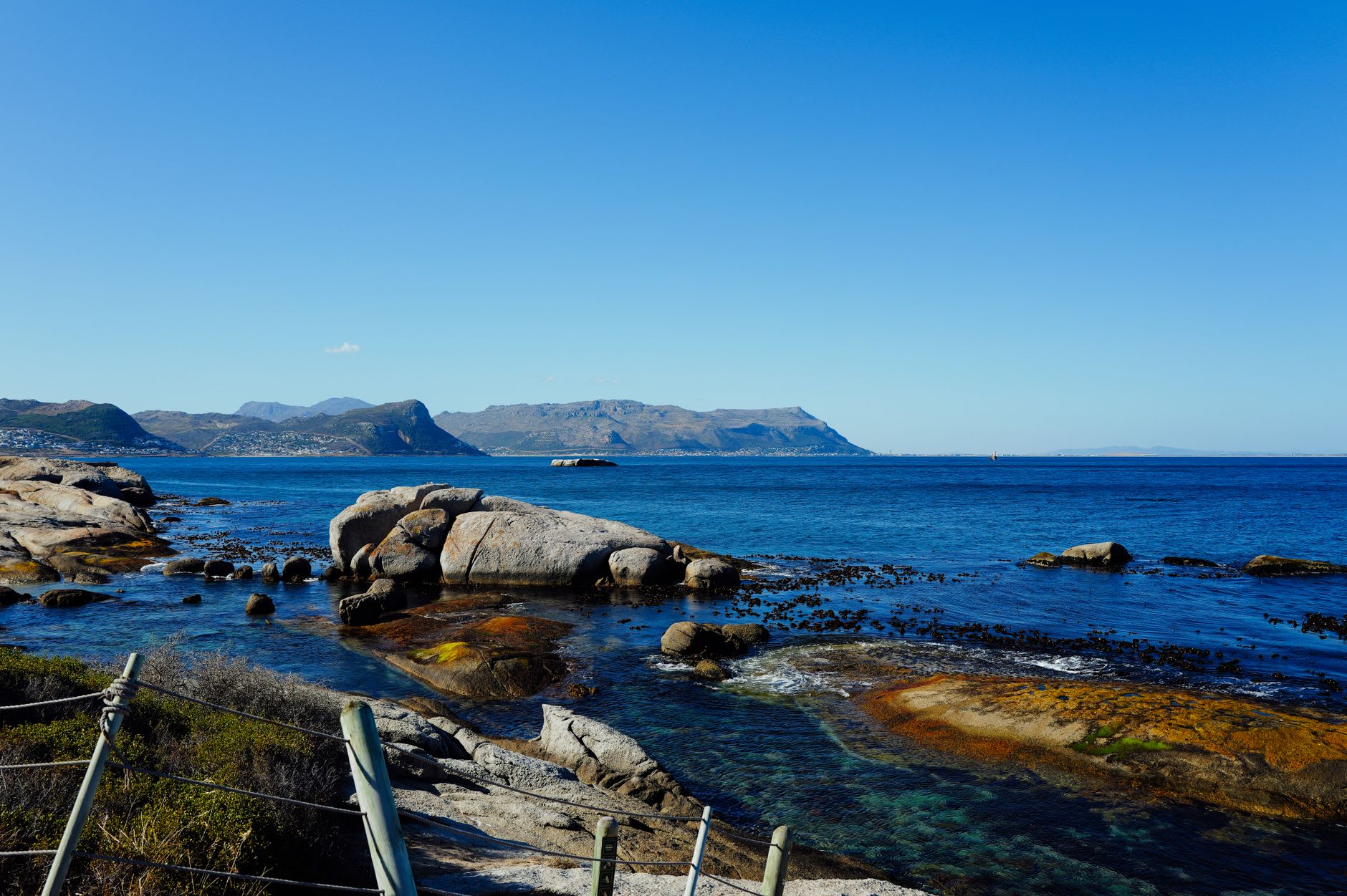 Surfers paddling out through the white water at Kommetjie Point with a large Atlantic swell feathering on the horizon