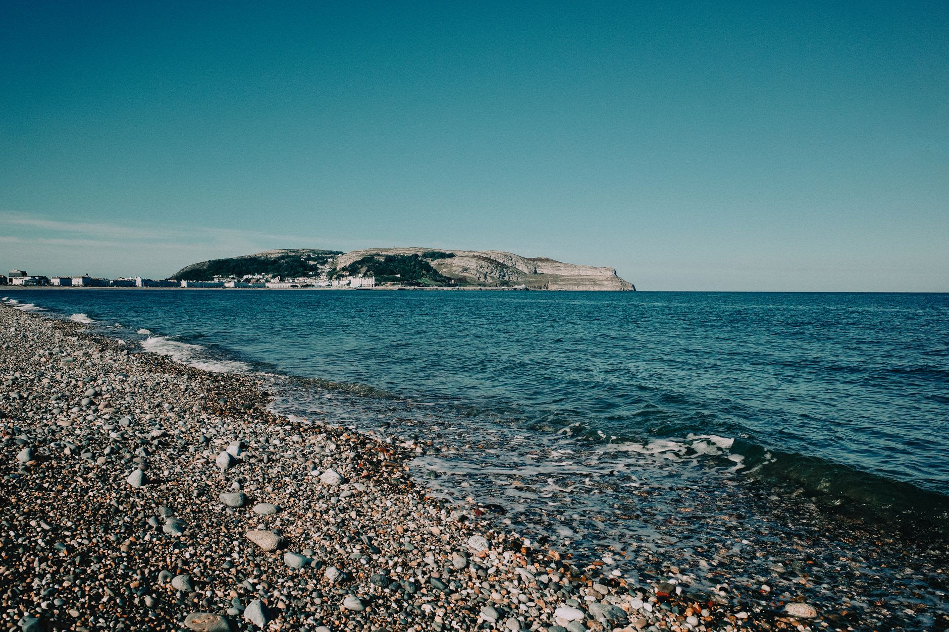 The white sand of Llandudno beach scattered with enormous smooth granite boulders, the cold blue Atlantic breaking in white foam, mountains framing the cove