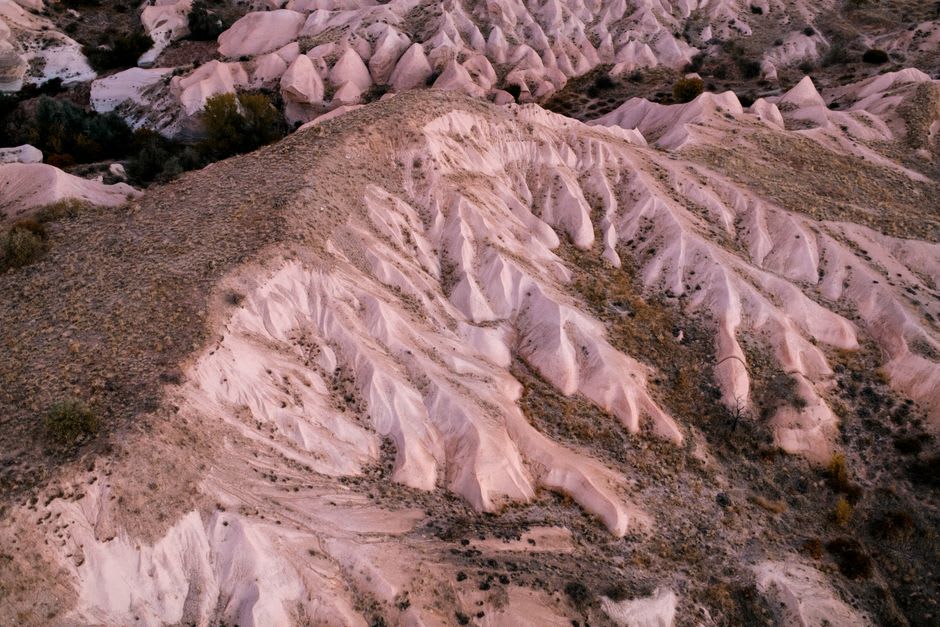 The pinkish, eroded fairy chimneys of Devrent Valley stretching toward the horizon with no vegetation or shade