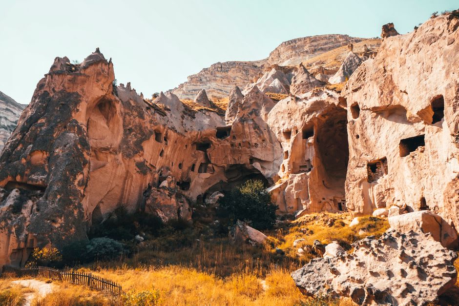 A rock-cut Byzantine church carved into the cliff face of Pancarlık Valley, its cruciform interior partially lit by a narrow entrance