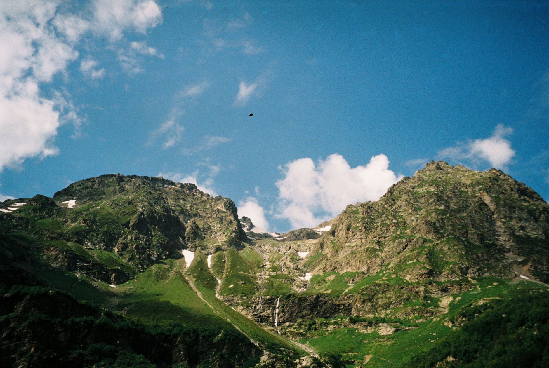 The ruined towers of Dariali fortress seen from the road below, the canyon walls pressing close on both sides with the Terek visible as a white line far beneath