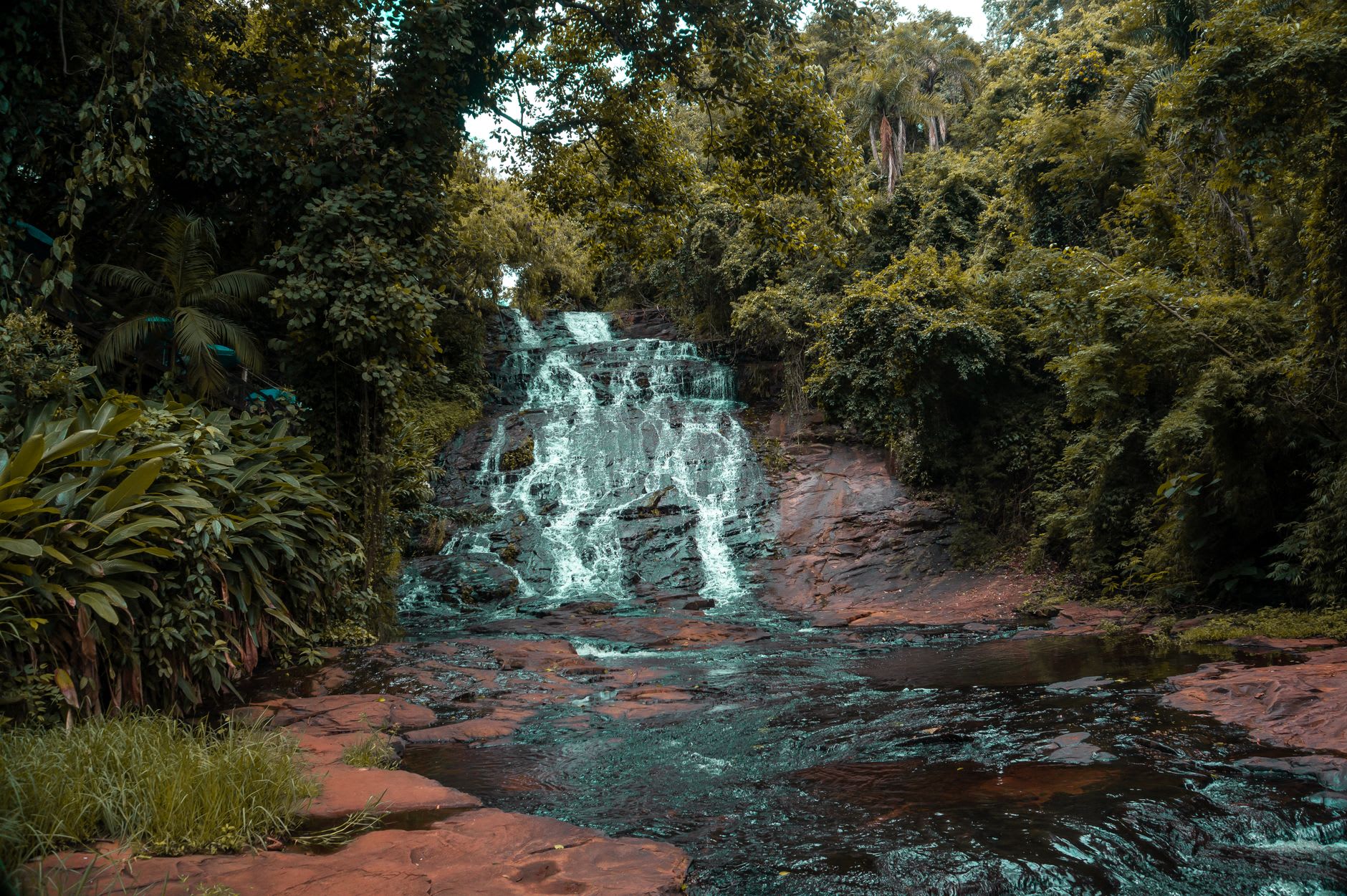 The full width of Boali Falls seen from the main viewpoint, red-brown water crashing into the gorge below in heavy flow
