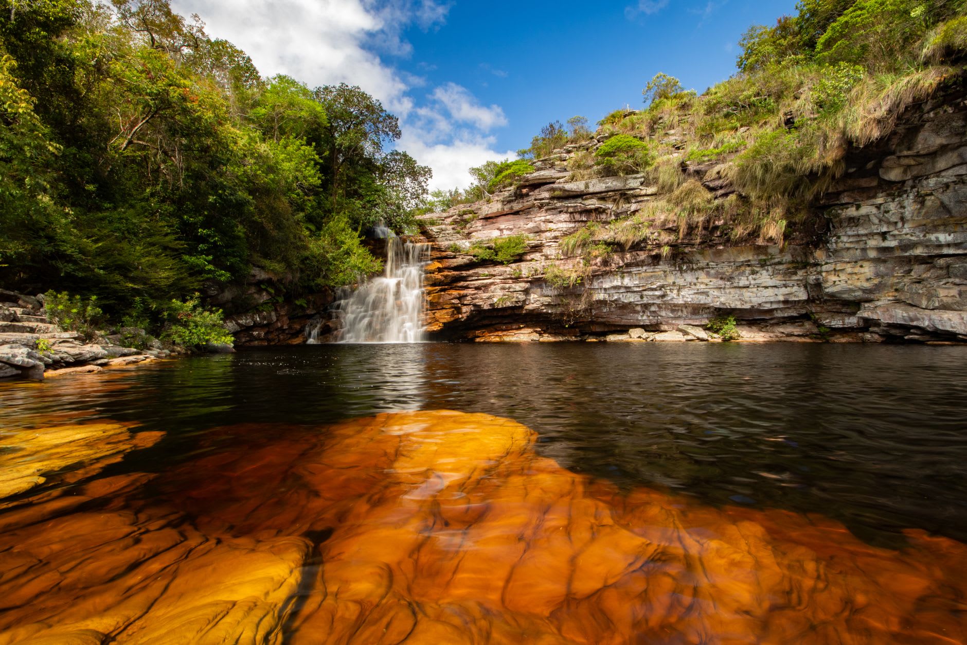 Natural rock slides at Cachoeira dos Couros with swimmers descending smooth quartzite into the turquoise pool below