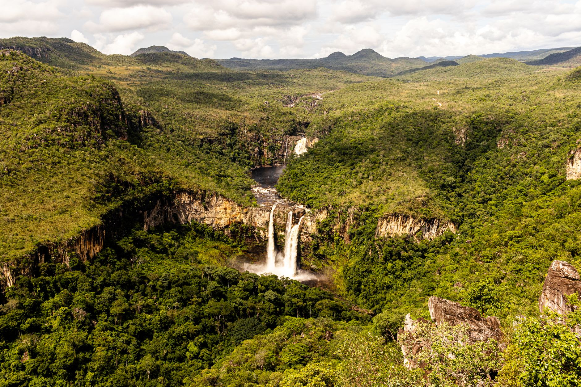 The approach trail to Cachoeira Santa Bárbara through open cerrado, red laterite path between twisted trees, the sky enormous and pale blue overhead