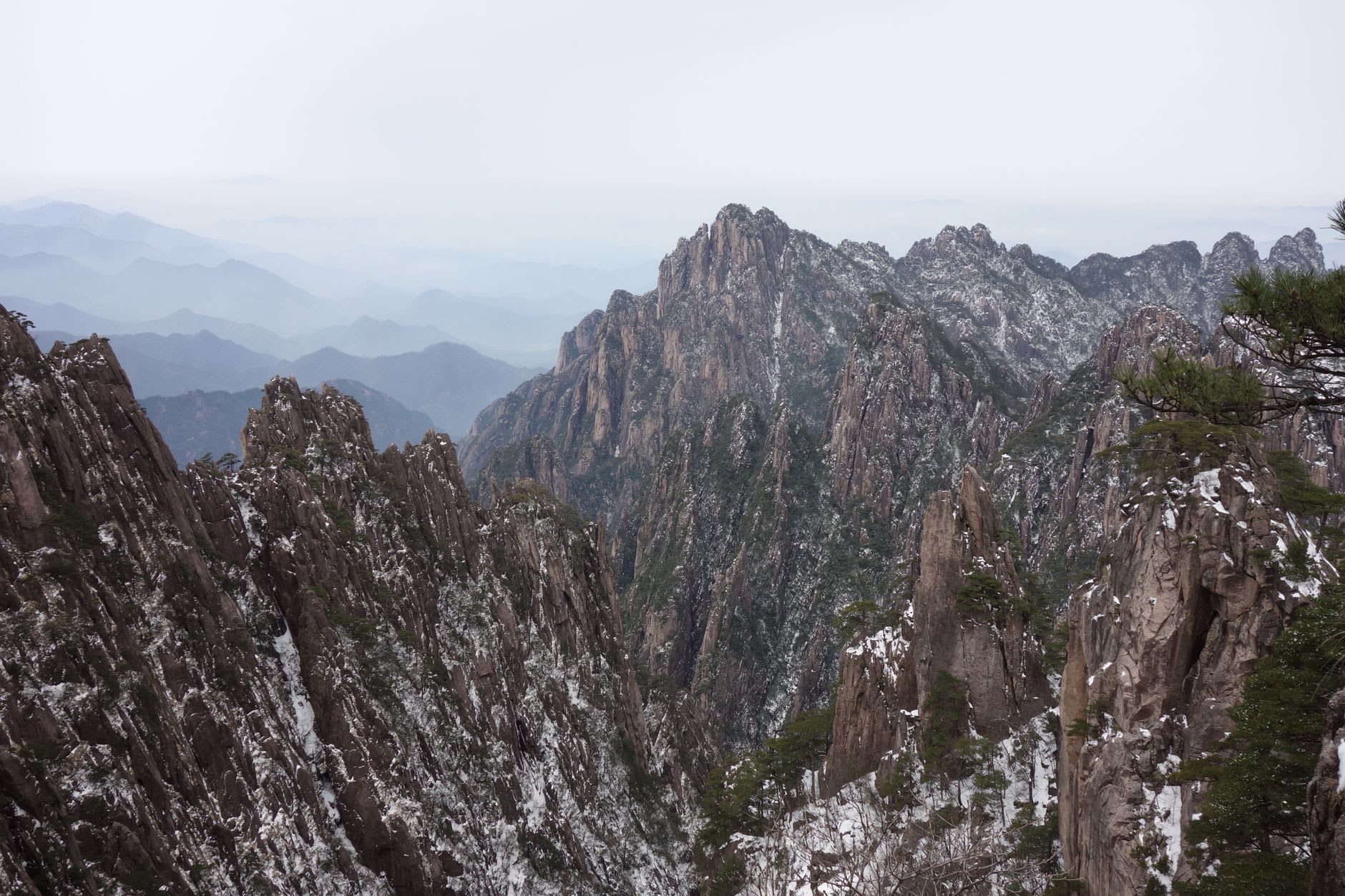 Stone staircase cut into a granite cliff winding between sheer peaks at Huangshan, with twisted pines clinging to the rock, Anhui, China