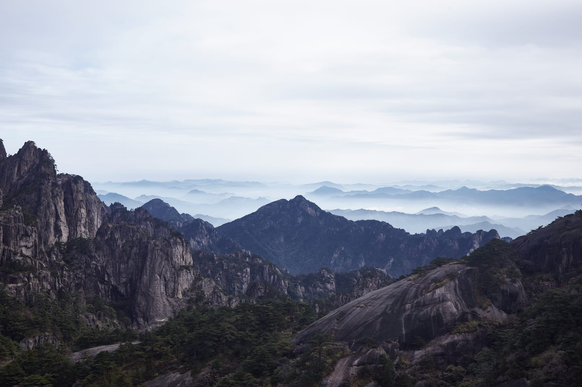 A crowd of visitors gathered on a summit viewpoint at dawn watching the sun rise over the cloud sea at Huangshan, China