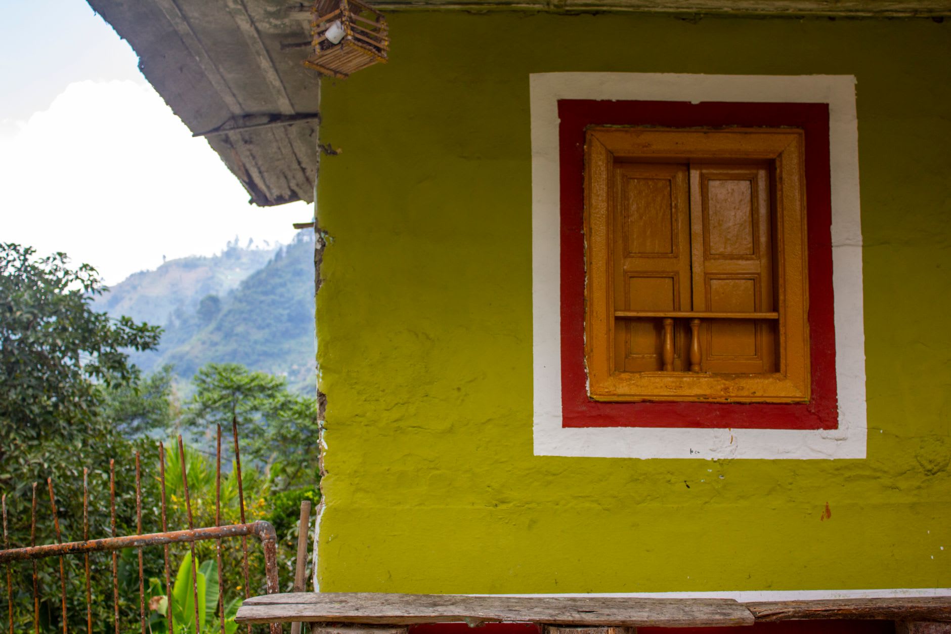 A farmer's front porch in Buenavista, traditional wooden chairs and a cloth filter coffee setup, the Quindío valley visible through the door