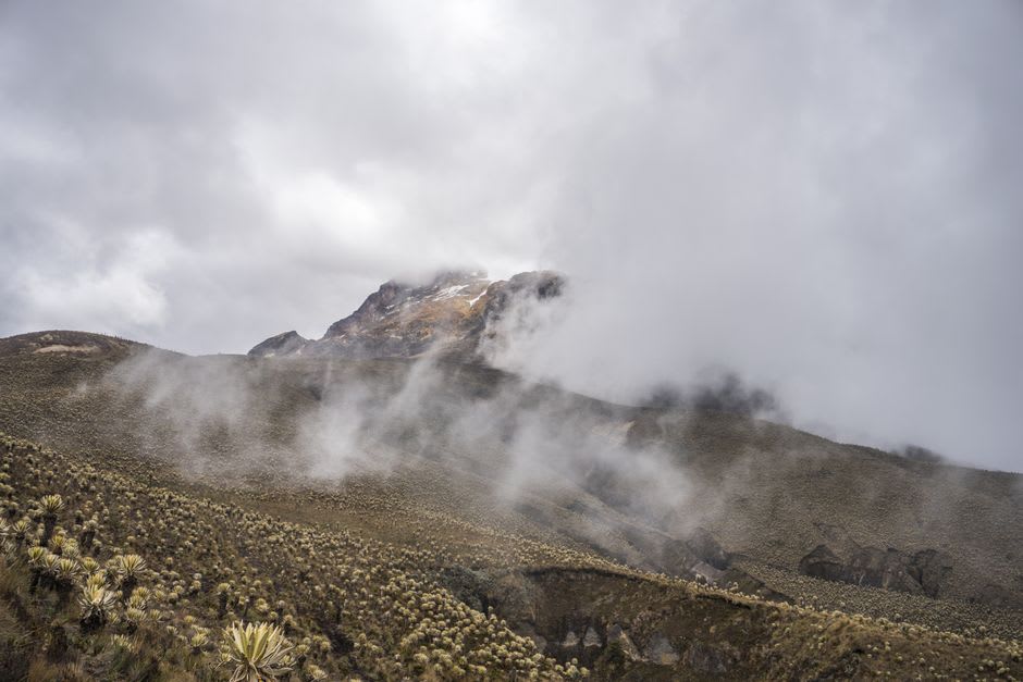 Hikers crossing a rocky trail with Nevado del Tolima visible in the distance