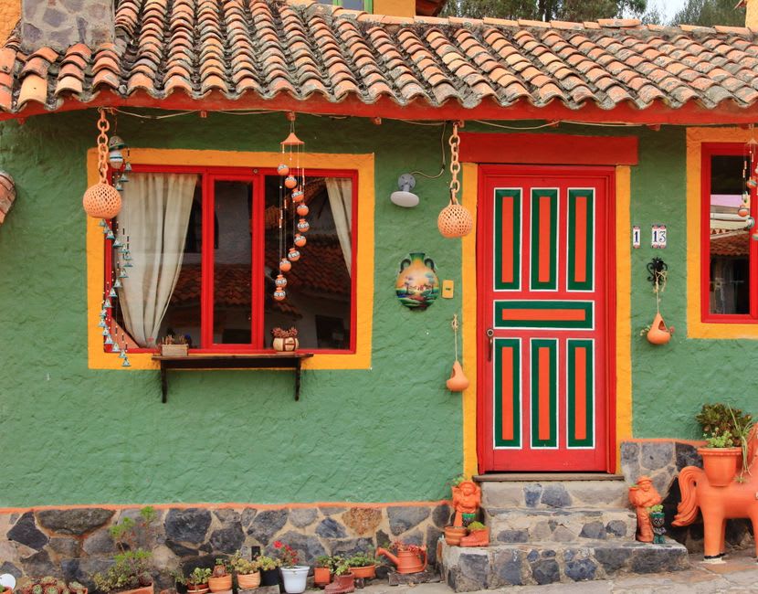 A pastel yellow and turquoise house facade on a Pijao street, framed by hanging plants