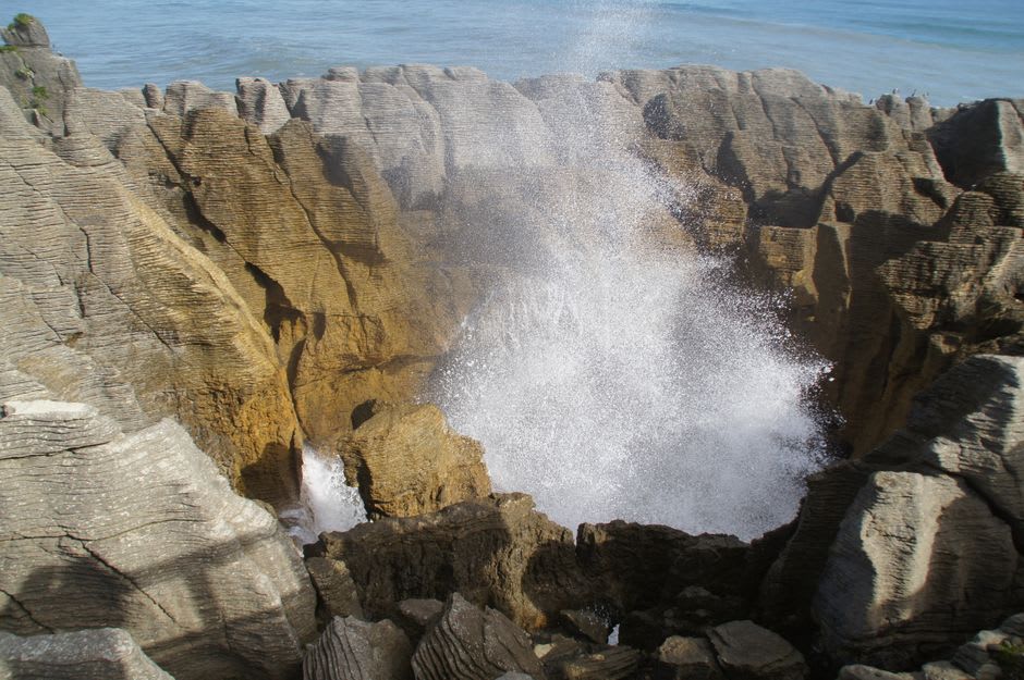 Waves crashing through a narrow volcanic channel at Trou du Prophète, sending spray over black basalt rock