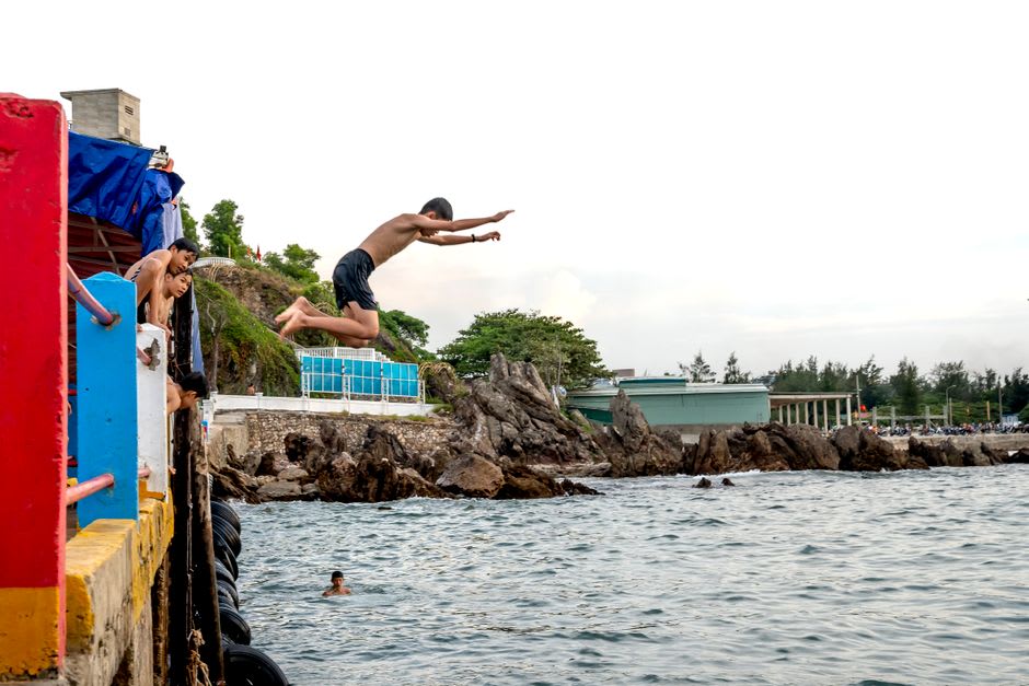 Local teenagers cliff jumping from the volcanic ledges at Black Rock into the surf below