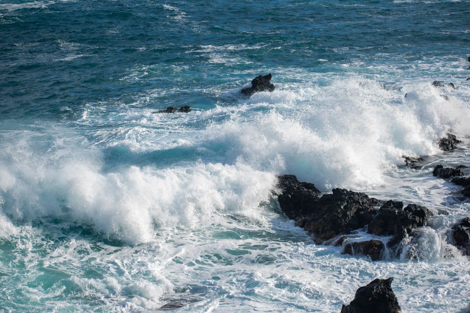 Waves breaking against the dark volcanic rocks of Black Rock during a vivid Rarotonga sunset