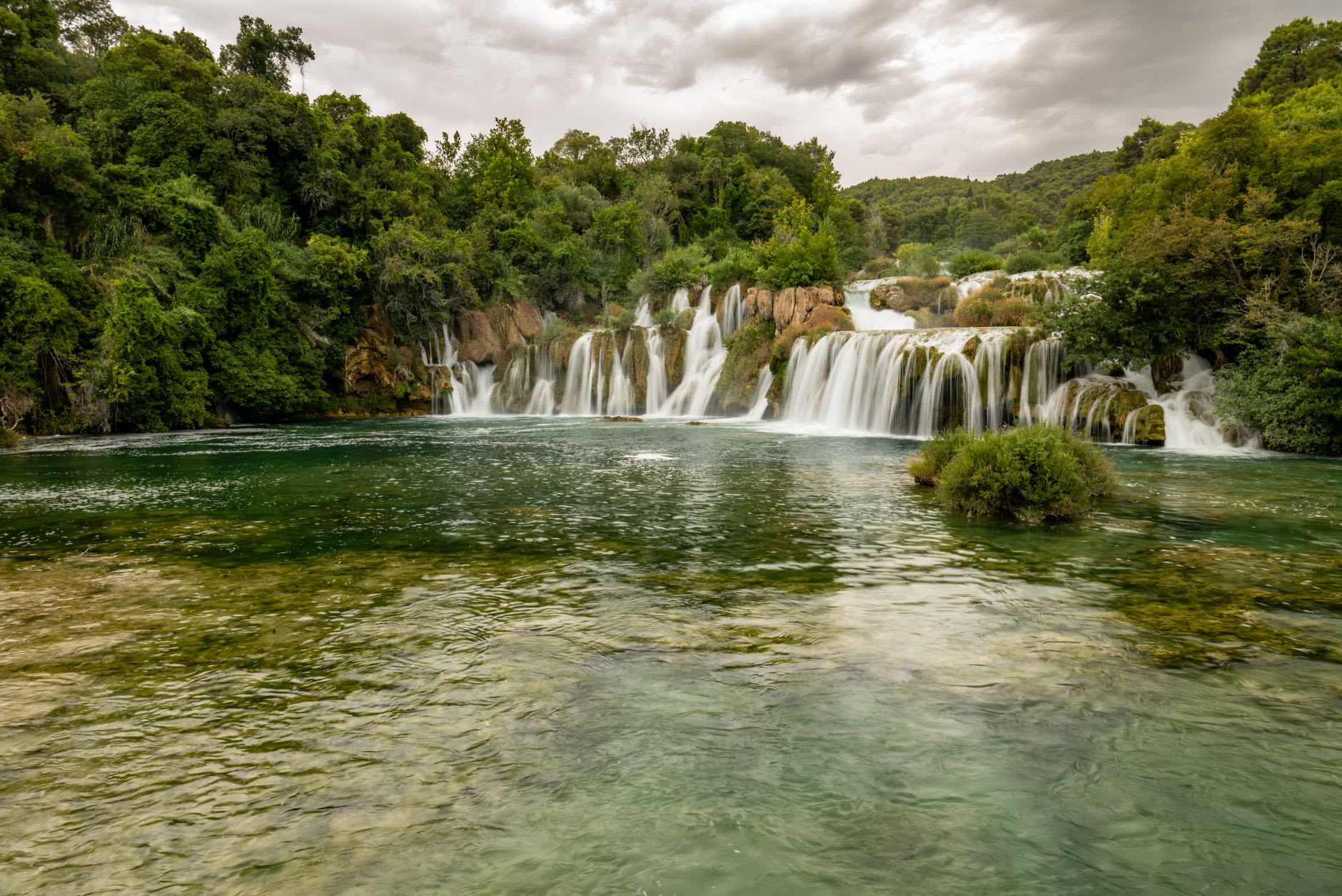 The wooden boardwalk crossing in front of the terraced cascades of Skradinski Buk, mist rising from the falling water