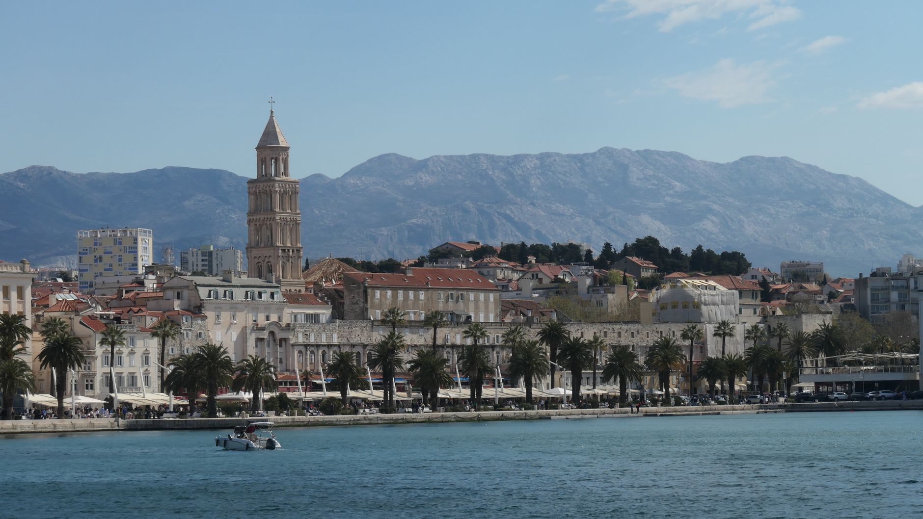 La pointe de la péninsule de la vieille ville de Korčula en soirée, remparts de pierre plongeant dans une eau transparente, montagnes dorées à l'horizon
