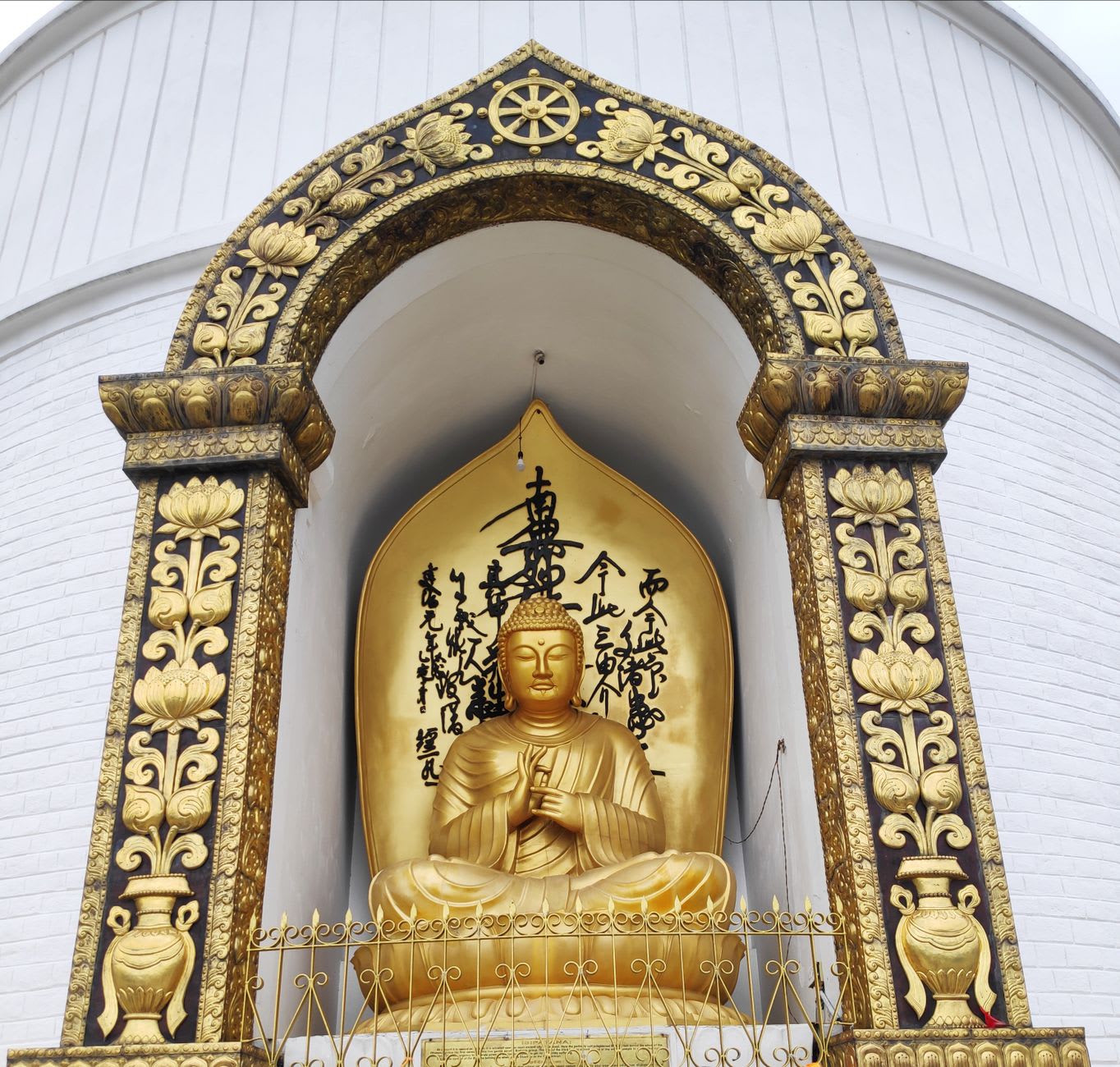 A Japanese monk in white robes seated at the base of the Peace Pagoda beating a prayer drum in the morning mist, Darjeeling, India