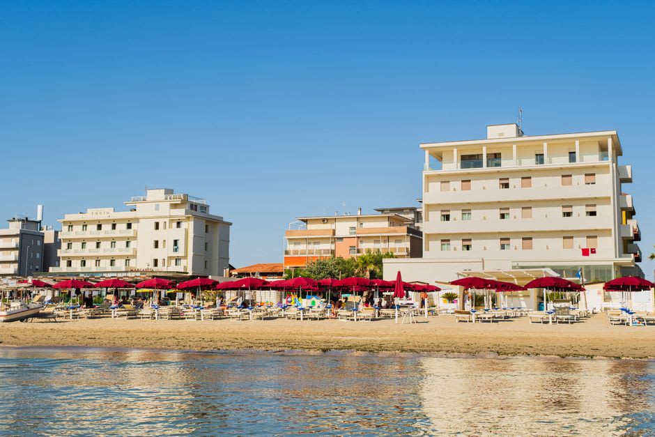 Des transats et des parasols alignés sur le rivage d'Ein Bokek, des tours d'hôtels visibles le long du front de mer à l'arrière-plan